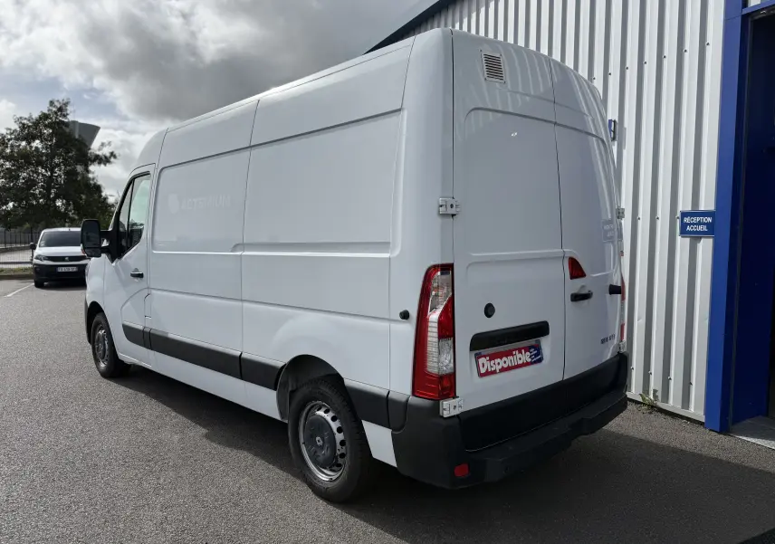 Vue 3/4 arrière droite d’un utilitaire Renault Master blanc stationné devant un bâtiment industriel.