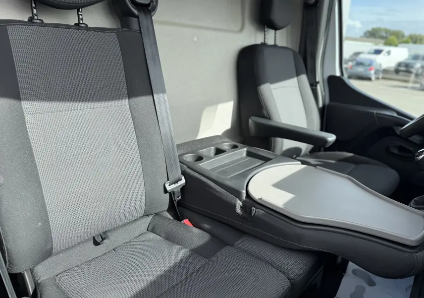 Vue intérieure côté conducteur du Renault Master blanc 2020, montrant les sièges gris avec accoudoir et tablette centrale rabattable.