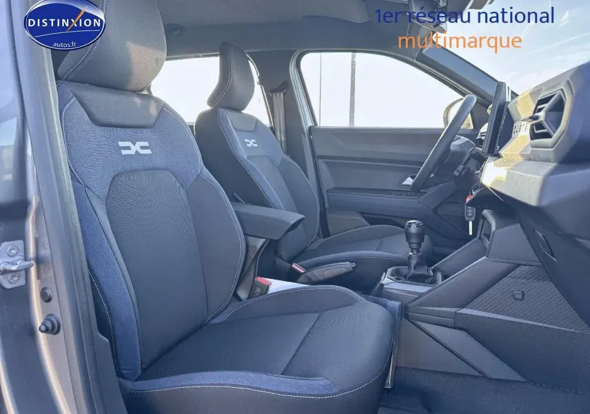 Vue intérieure côté conducteur du Dacia Duster 2025 avec sièges tissu gris et accoudoir central avant.