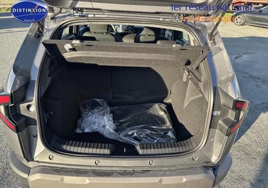 Coffre ouvert vu de l'arrière d'un Dacia Duster gris schiste 2025, montrant l'espace de chargement vide avec cache-bagages relevé.