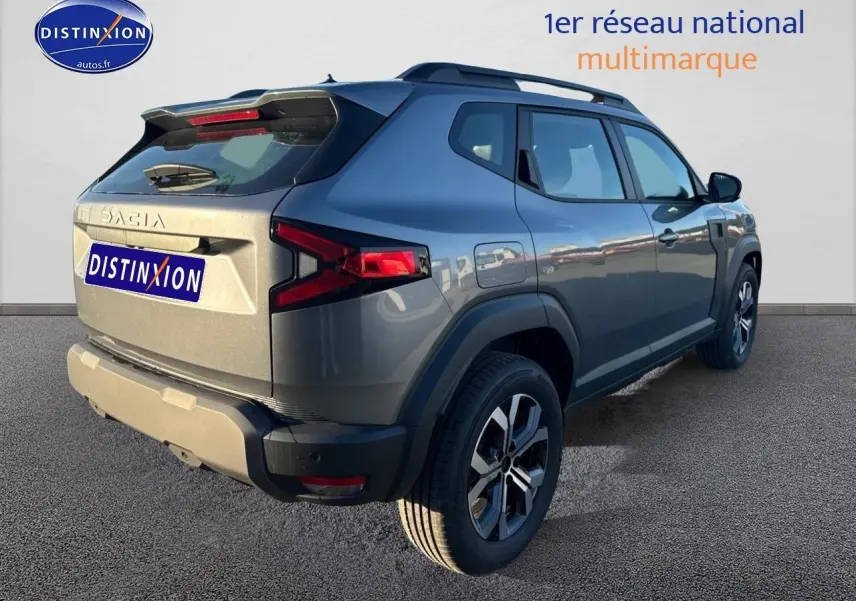 Vue 3/4 arrière droite du Dacia Duster gris schiste avec barres de toit et jantes alu distinctives.
