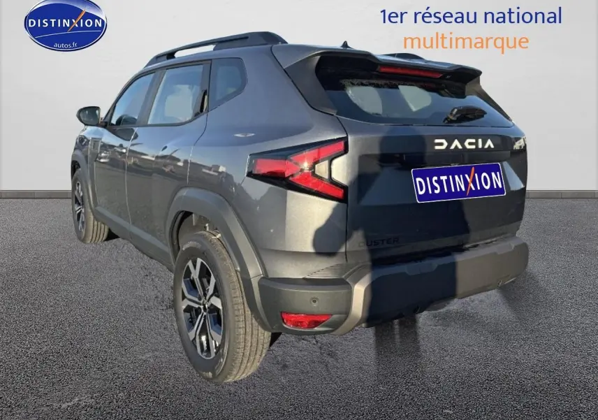 Vue 3/4 arrière droite du Dacia Duster gris schiste avec jantes alu et barres de toit visibles.