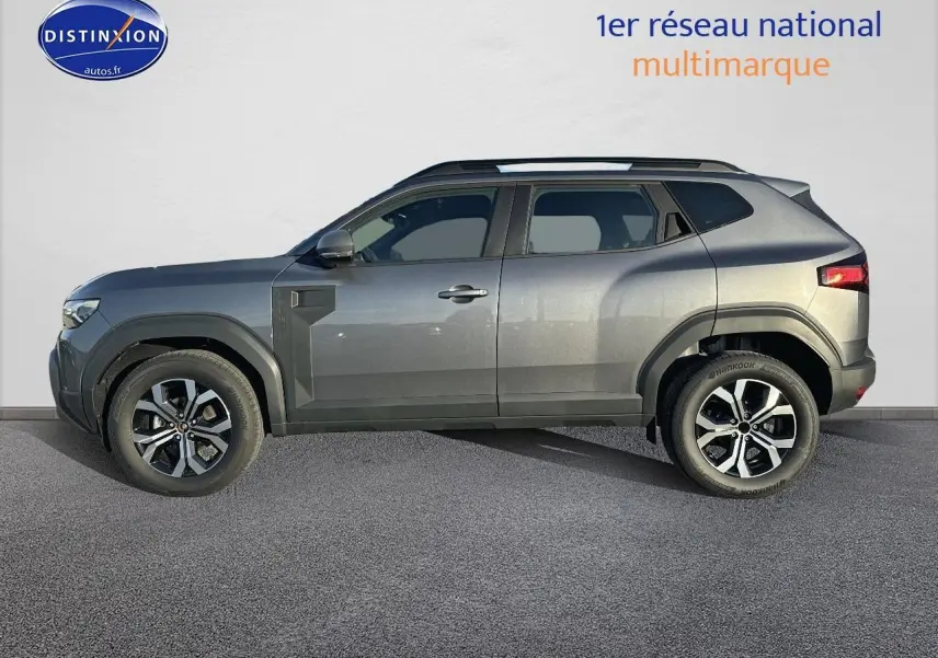 Vue de profil côté gauche d'un Dacia Duster gris schiste 2025 avec jantes alu et barres de toit noires.