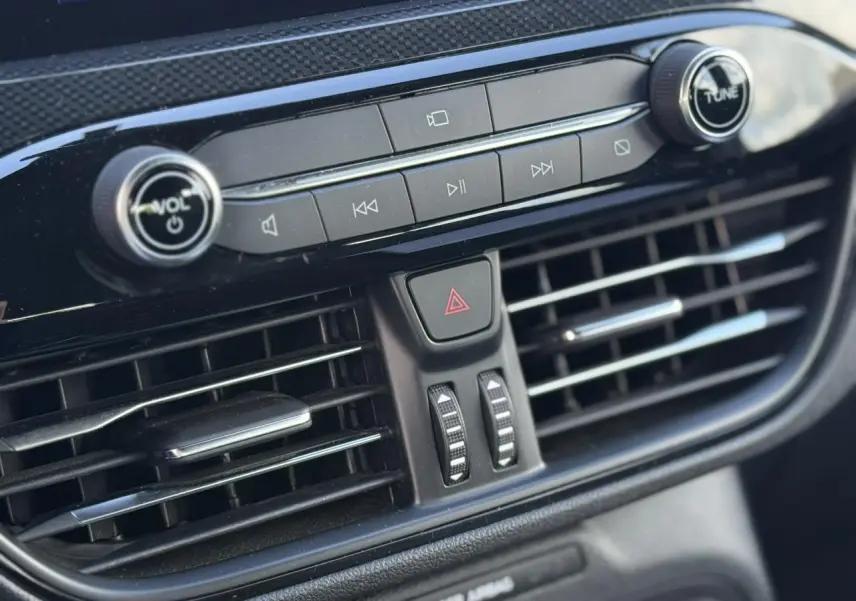 Gros plan sur la console centrale noire du Ford Kuga 2024, avec commandes audio et aérateurs horizontaux.