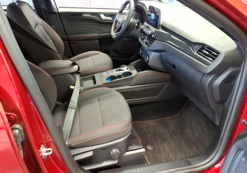 Vue intérieure côté conducteur du Ford Kuga rouge Lucifer 2024, avec sièges noirs et surpiqûres rouges, tableau de bord moderne.