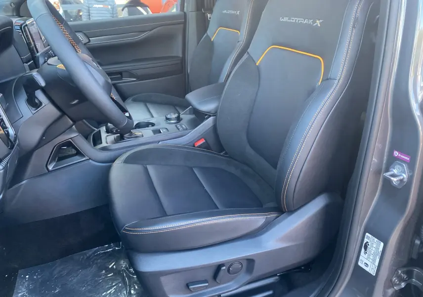 Vue intérieure côté conducteur du Ford Ranger Wildtrak X 2025 gris carbone, sièges en cuir noir avec surpiqûres orange et logo brodé.