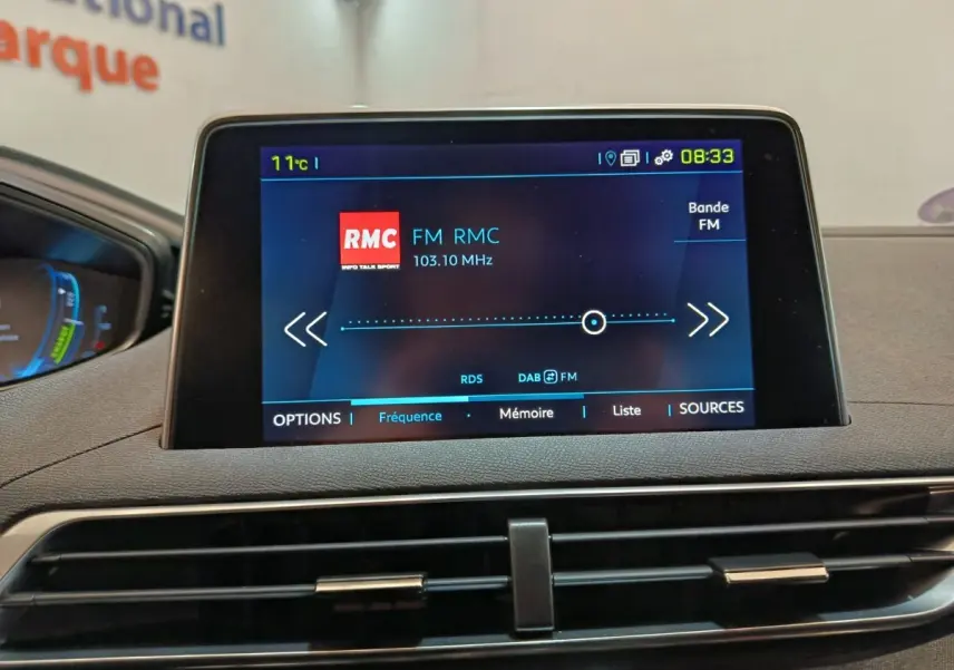 Écran tactile central affichant la radio FM RMC dans l’habitacle du Peugeot 3008 bleu, vue de face.