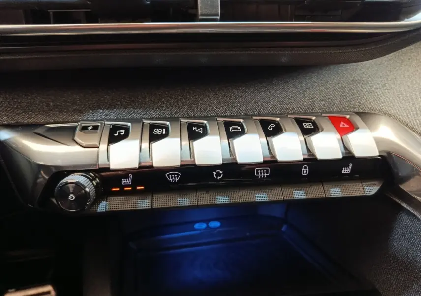 Gros plan sur la console centrale avec les boutons piano argentés et le bouton rouge de warning du Peugeot 3008 bleu hybride.