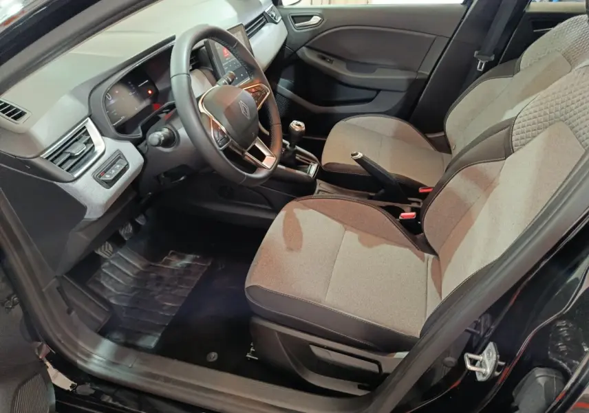 Intérieur avant droit de la Renault Clio noire 2025, montrant sièges tissu gris, volant multifonctions et boîte manuelle.