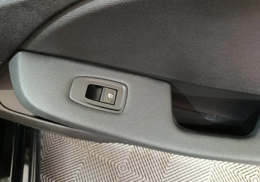 Gros plan sur le bouton de commande de la vitre électrique côté conducteur dans une Renault Clio noire, intérieur sobre.