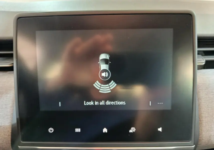 Écran tactile central de la Renault Clio noir affichant l'aide au stationnement avec vue du véhicule et alertes sonores.