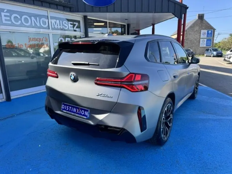 BMW X3 xDrive20 M Sport gris métallisé vue 3/4 arrière avec feux LED et jantes sport sur parking bleu.