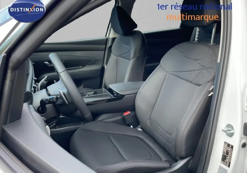 Vue intérieure côté conducteur du Hyundai Tucson blanc Atlas 2026, mettant en valeur les sièges tissu noir et le volant multifonction.