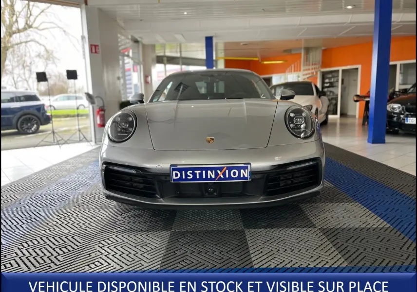 Vue frontale d'une Porsche 911 (992) Coupé argent GT exposée en showroom avec plaque Distinxion visible.