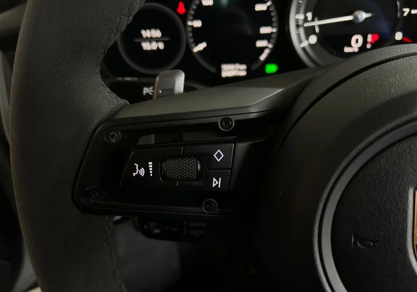 Gros plan sur les commandes gauche du volant en Alcantara noir de la Porsche 911 Carrera S 2019, avec tableau de bord digital en arrière-plan.