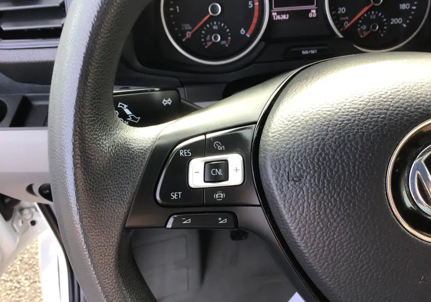 Gros plan sur le volant noir du Volkswagen Crafter blanc, montrant les commandes de régulateur de vitesse à gauche.
