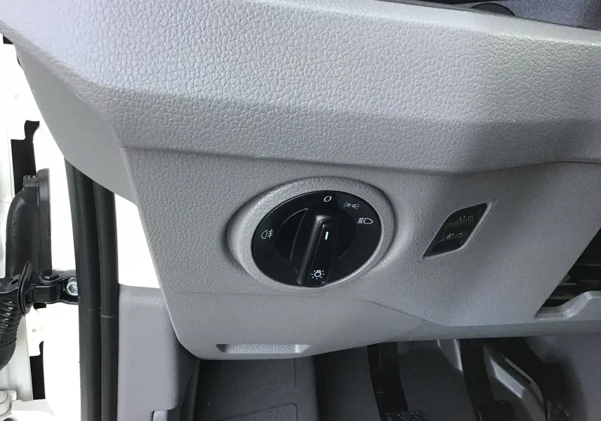 Gros plan sur le bouton de commande des phares dans l'habitacle gris clair du Volkswagen Crafter blanc L3H3 2021.