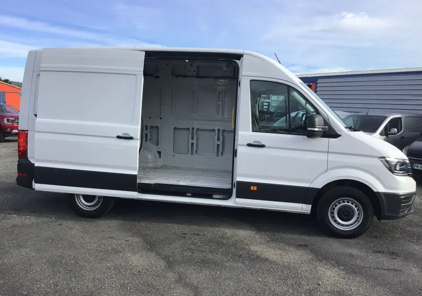 Vue latérale droite d'un Volkswagen Crafter blanc avec porte coulissante ouverte dévoilant l'intérieur vide du fourgon.