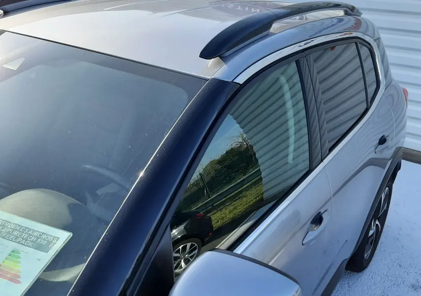 Vue en plongée du côté gauche du Citroën C5 Aircross gris Artense avec barres de toit noires et vitres teintées.