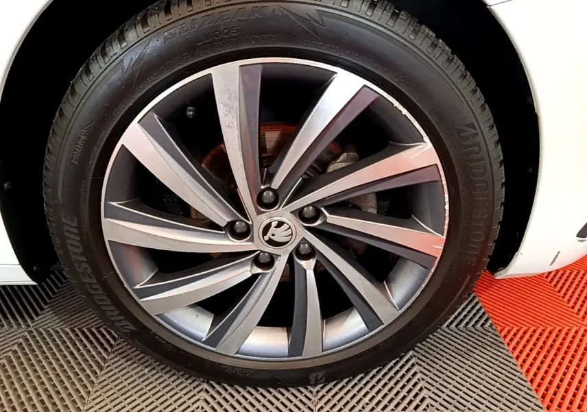 Gros plan sur la roue avant droite d’une Skoda Octavia blanche, jante alliage gris foncé à 5 doubles branches.