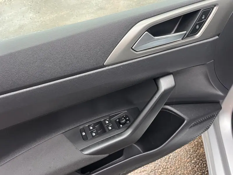 Vue rapprochée de la porte avant gauche grise d'une Volkswagen Polo 2021, avec commandes électriques et poignée intégrée.