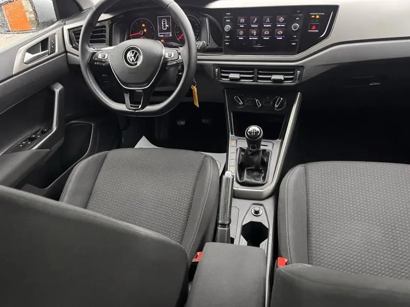 Vue intérieure avant de la Volkswagen Polo 1.0 gris Urano, avec volant cuir multifonction et levier de vitesse manuel.
