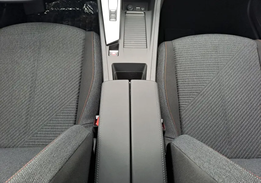 Vue plongeante sur la console centrale et les sièges avant en tissu gris avec surpiqûres orange du Peugeot 308 2025.