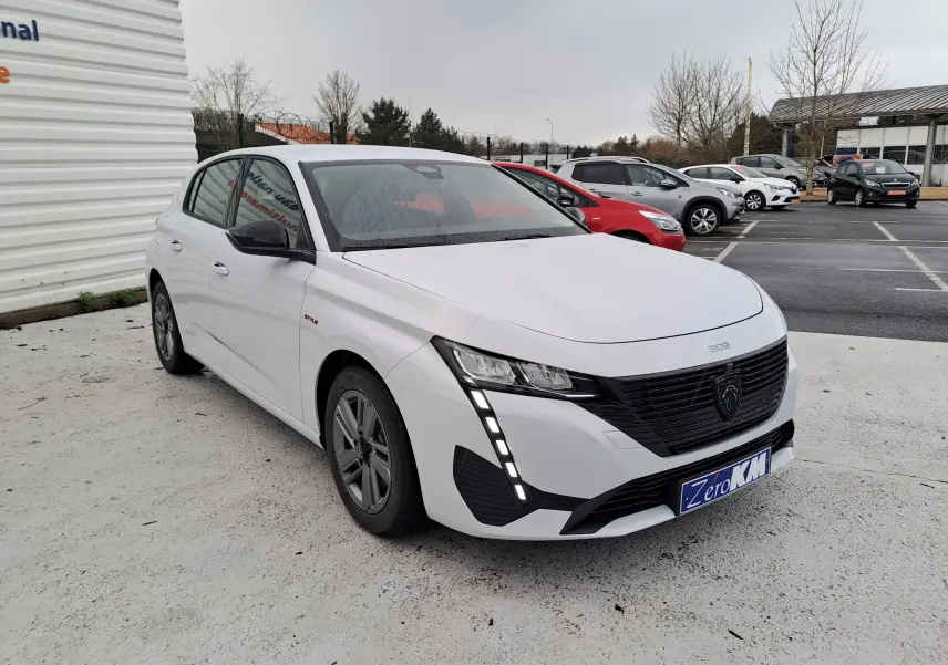 Peugeot 308 blanc Okenite vue 3/4 avant gauche, avec calandre noire et feux LED verticaux distinctifs.