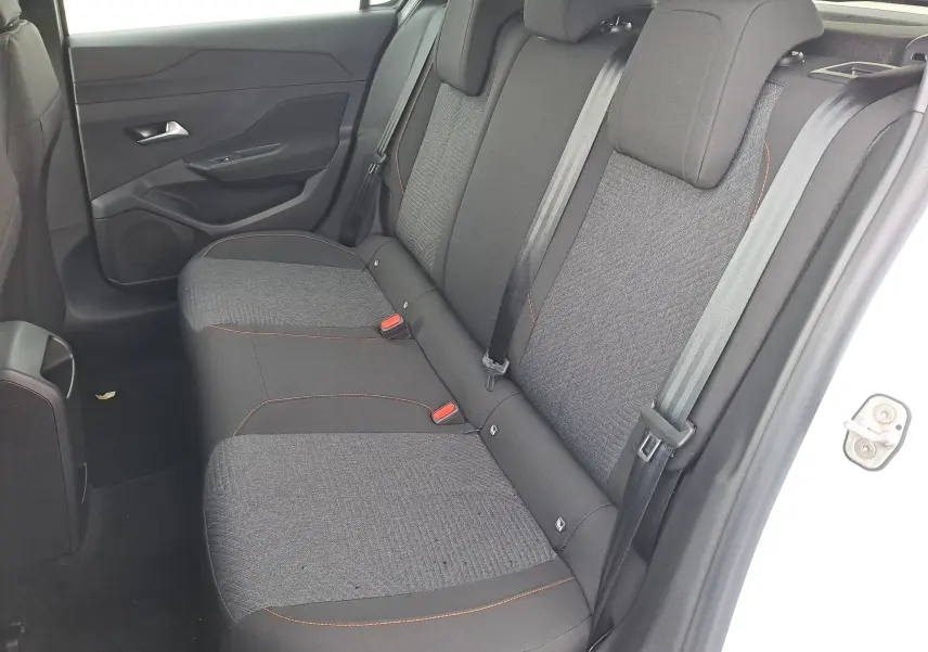 Vue intérieure côté droit des sièges arrière gris foncé avec surpiqûres orange d'une Peugeot 308 blanche 2025.