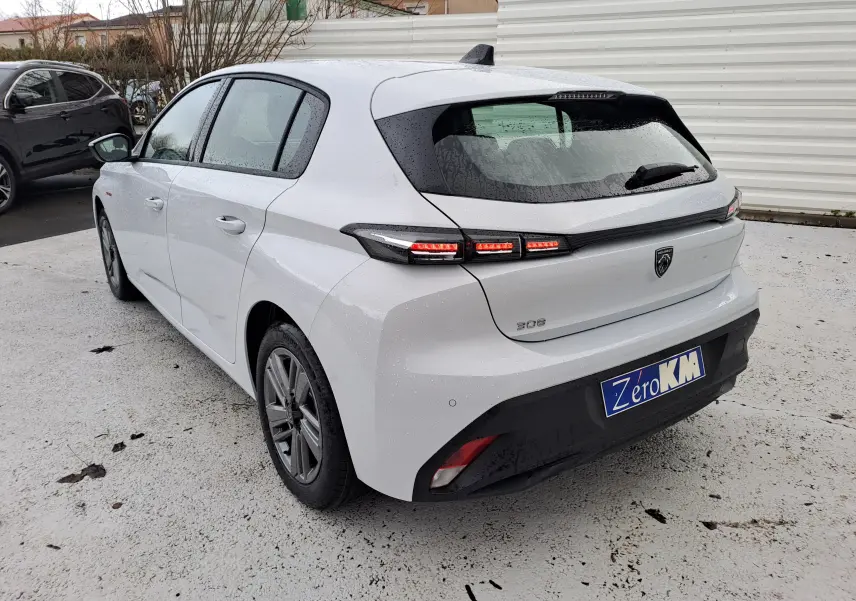 Vue 3/4 arrière droite d'une Peugeot 308 blanche Okenite avec feux arrière allumés et plaque d'immatriculation Zero KM.