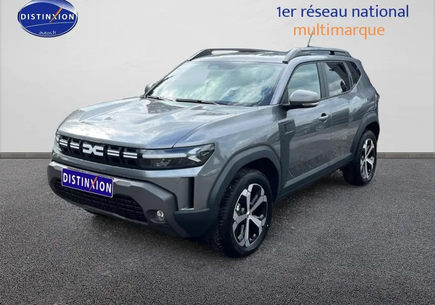 Dacia Duster gris schiste en 3/4 avant droit, avec barres de toit et jantes alliage distinctives.