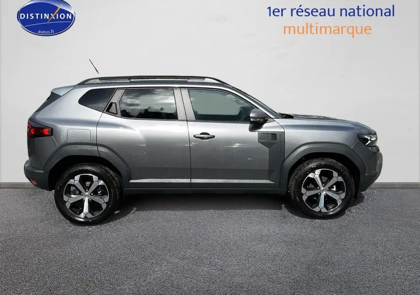 Profil droit du Dacia Duster gris schiste 2025 avec jantes alu et barres de toit visibles sur fond neutre.