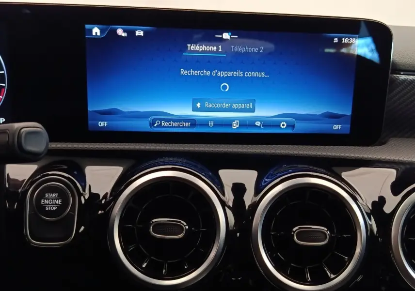 Vue rapprochée du tableau de bord noir brillant de la Mercedes Classe A 250 e Hybrid avec écran tactile bleu et boutons circulaires d’aération.