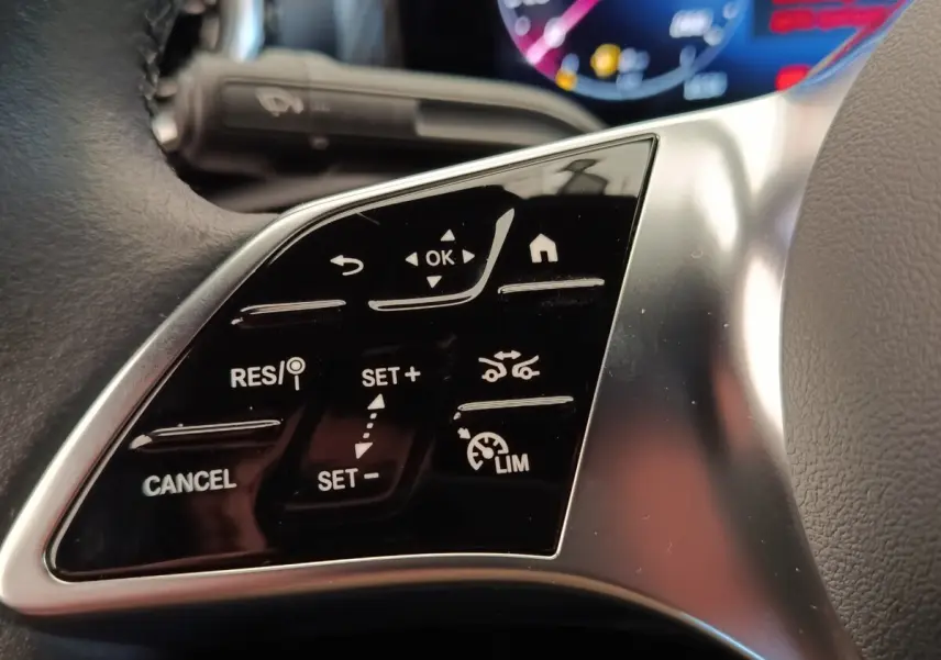Gros plan sur les commandes multifonctions noires du volant côté gauche d’une Mercedes Classe A 250 e hybride 2024.