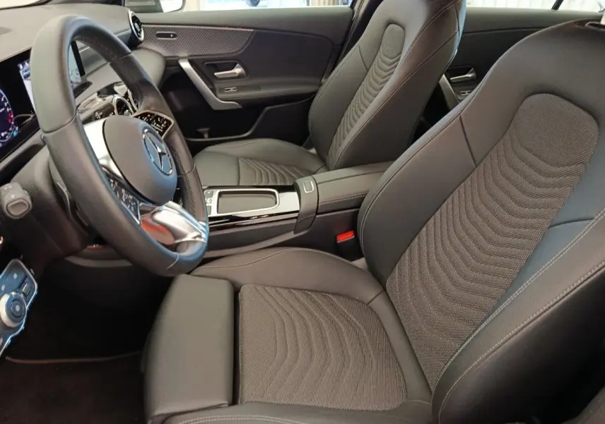 Vue intérieure côté conducteur de la Mercedes Classe A 250 e Hybrid avec sièges noirs et volant cuir multifonctions.