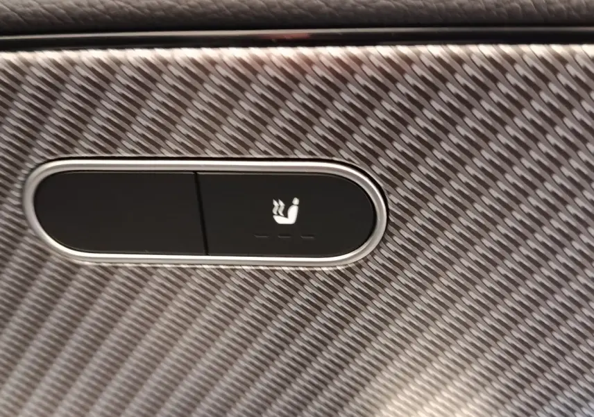 Gros plan sur le bouton de siège chauffant sur une surface à motif carbone à l'intérieur de la Mercedes Classe A 250 e Hybrid.