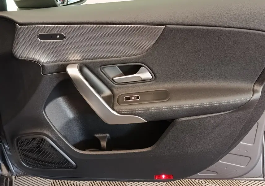 Porte intérieure côté gauche de la Mercedes Classe A 250 e Hybrid gris foncé avec garniture carbone et poignée argentée.