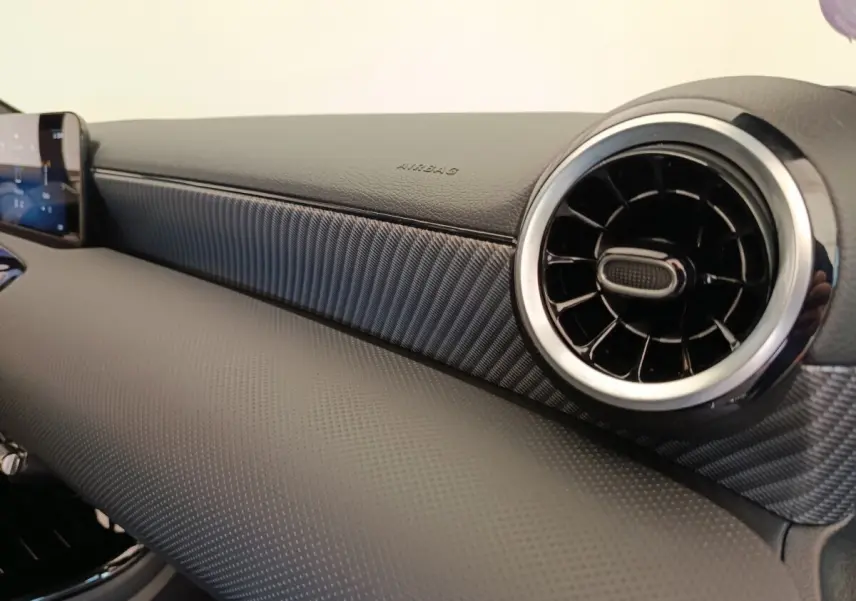Détail du tableau de bord noir avec sortie d'air ronde chromée et écran tactile dans une Mercedes Classe A 250 e Hybrid 2024.