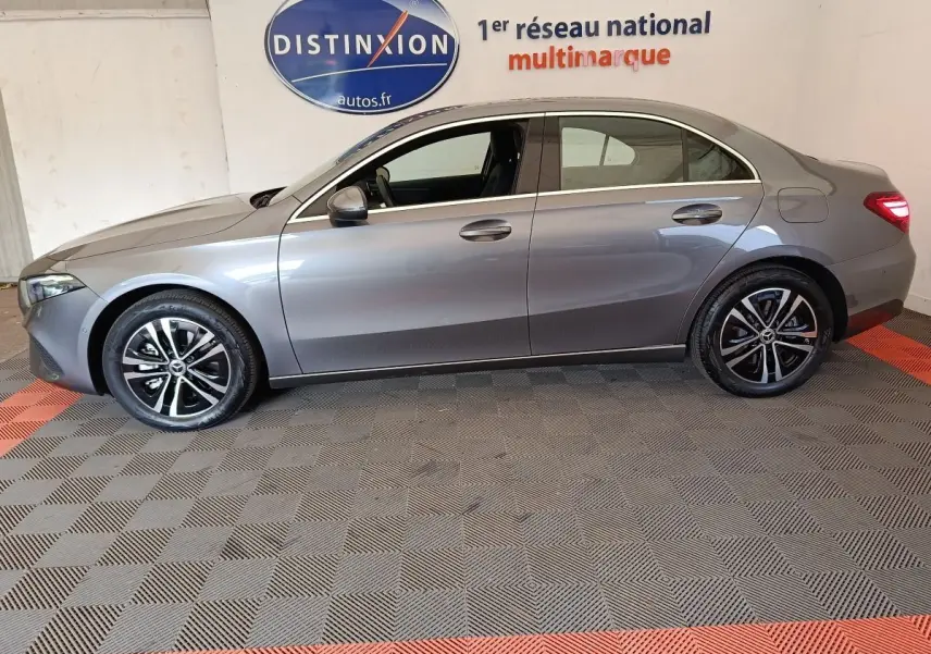 Profil droit d'une Mercedes Classe A 250 e Hybrid gris foncé, avec jantes alliage et feux arrière allumés en intérieur showroom.