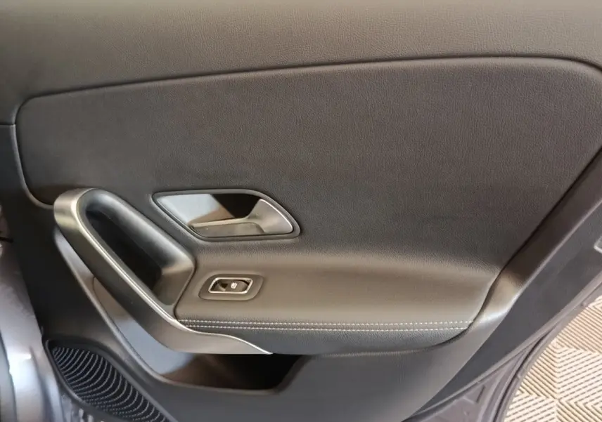 Gros plan sur la garniture intérieure de porte noire avec poignée argentée et bouton de commande de vitre, côté conducteur.