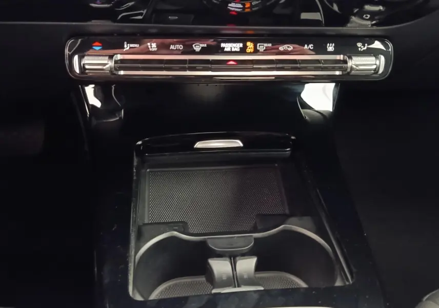 Vue rapprochée de la console centrale noire brillante avec commandes climatisation tactile et porte-gobelets d’une Mercedes Classe A 250 e hybride 2024.