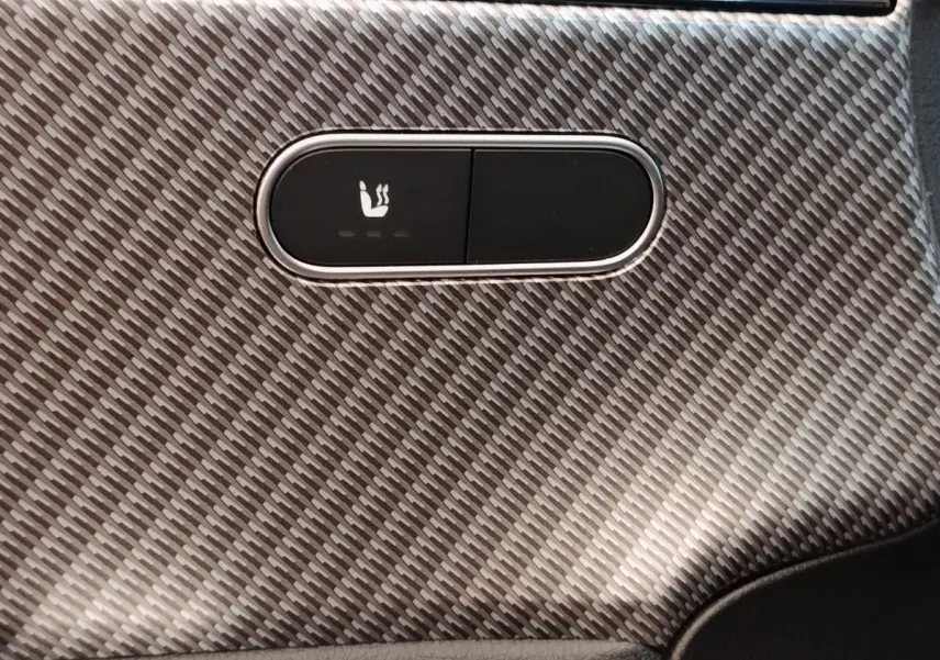 Détail du bouton de siège chauffant sur la garniture intérieure en fibre de carbone grise d'une Mercedes Classe A 250 e Hybrid 2024.