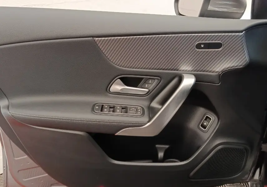 Vue intérieure côté gauche de la porte d’une Mercedes Classe A 250 e Hybrid gris foncé avec insert carbone et commandes électriques.