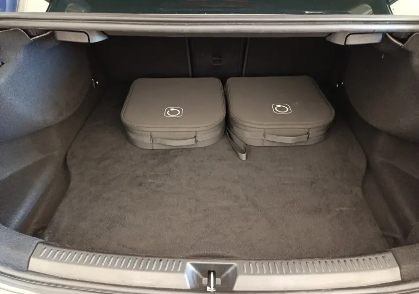 Coffre ouvert d’une Mercedes Classe A 250 e hybride gris foncé, avec deux sacs de charge posés à l’intérieur.