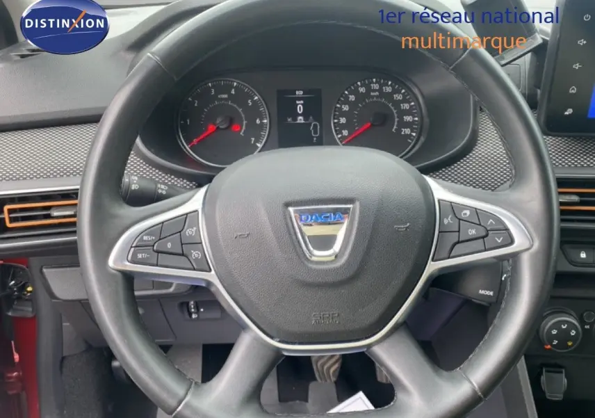 Vue rapprochée du volant noir de la Dacia Sandero 2022 avec tableau de bord et commandes visibles, intérieur rouge partiel.