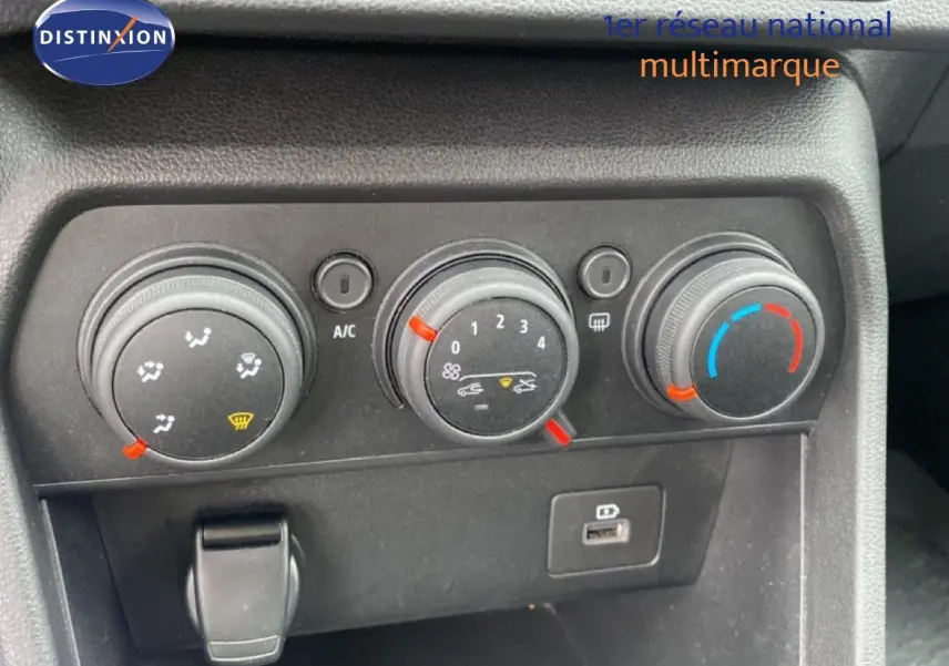 Gros plan sur les commandes de climatisation de la Dacia Sandero rouge fusion, avec réglages manuels et port USB visible.