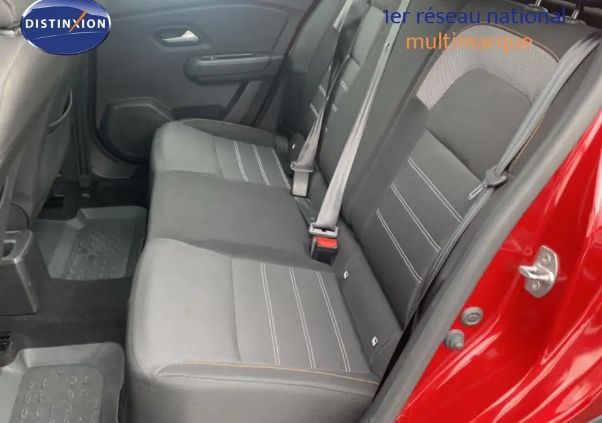 Vue intérieure arrière côté droit du Dacia Sandero rouge fusion, montrant les sièges tissu gris avec surpiqûres orange.
