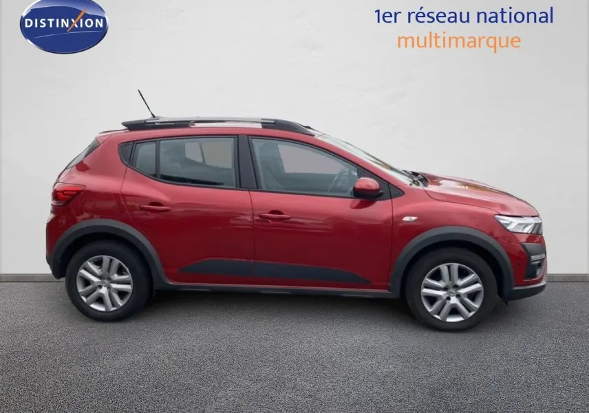 Vue latérale droite d'une Dacia Sandero Stepway rouge fusion métal avec barres de toit et protections noires.