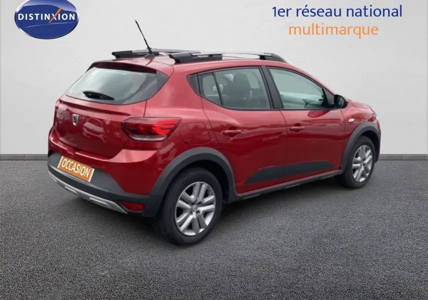 Vue 3/4 arrière droite d'une Dacia Sandero Stepway rouge fusion métal avec barres de toit et protections noires.
