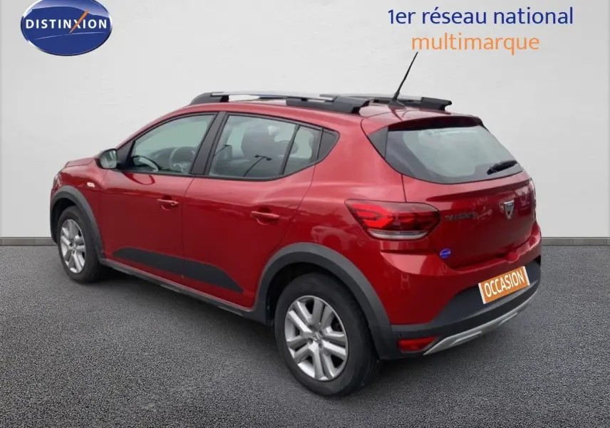 Vue 3/4 arrière droite d'une Dacia Sandero Stepway rouge fusion métal avec barres de toit et protections noires.